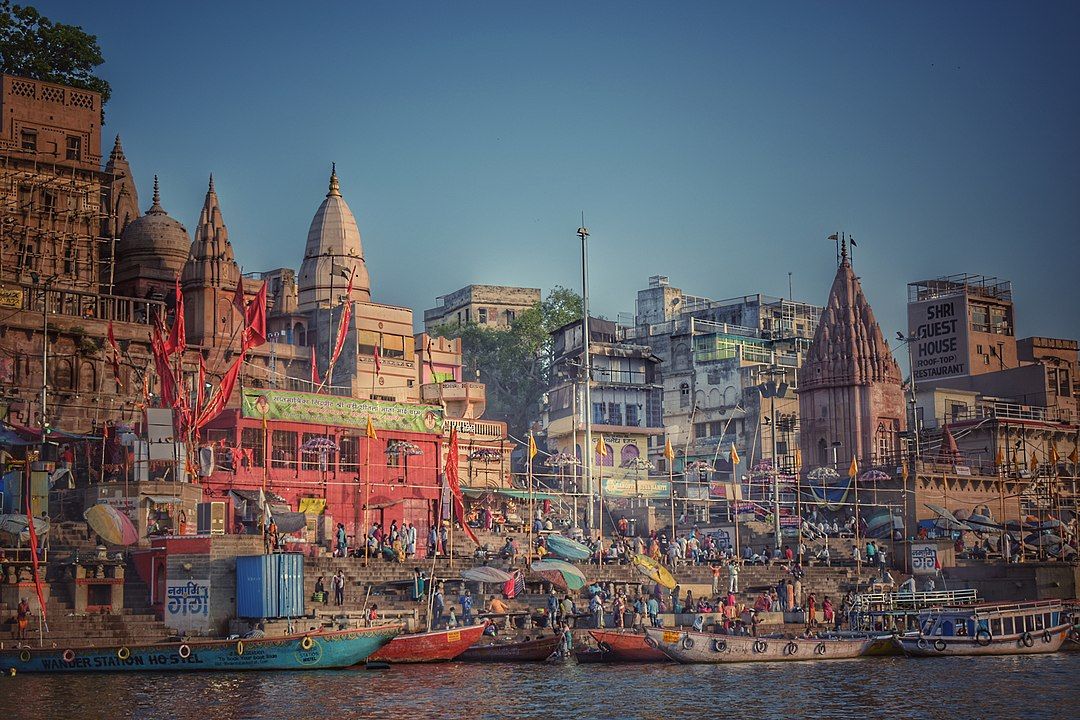 Vista panorámica de los ghats de Benares junto al río Ganges, con templos antiguos, barcos coloridos y multitudes de personas al atardecer