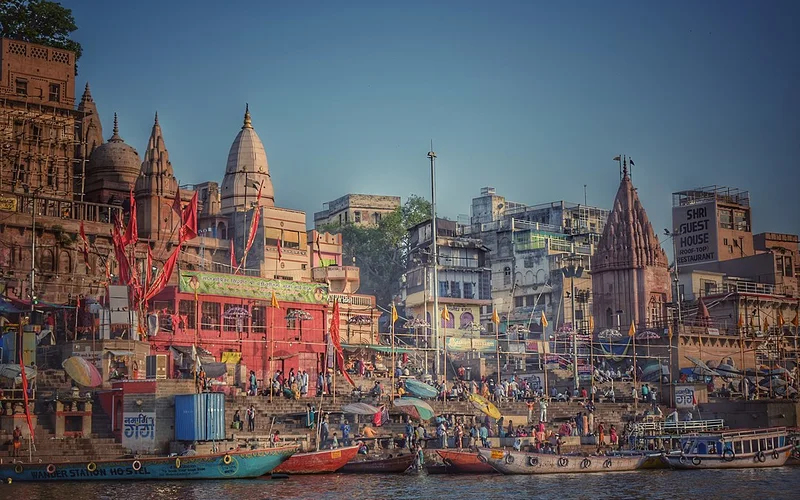 Vista panorámica de los ghats de Benares junto al río Ganges, con templos antiguos, barcos coloridos y multitudes de personas al atardecer