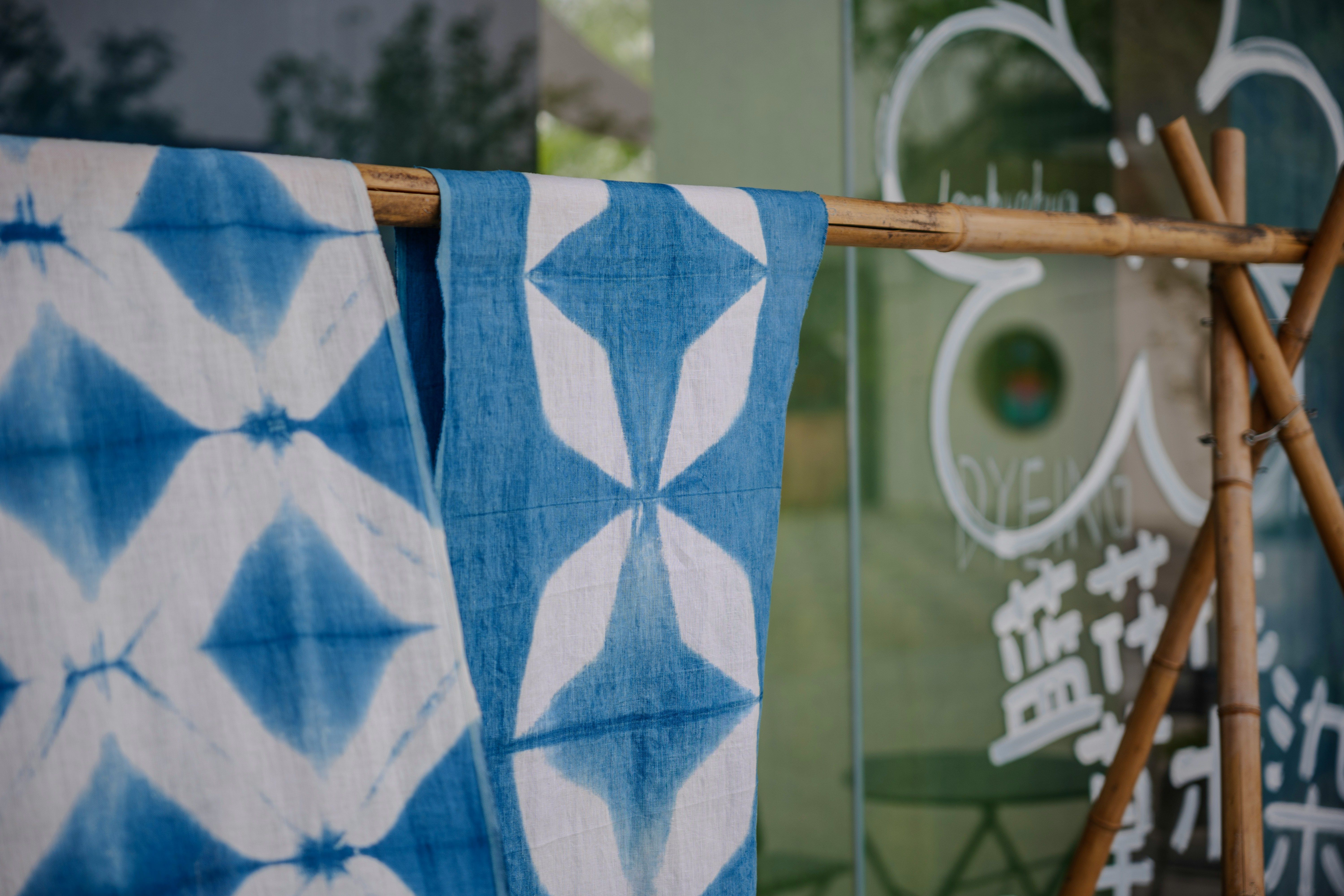 Telas shibori azules y blancas con patrones geométricos cuelgan de un soporte de bambú.