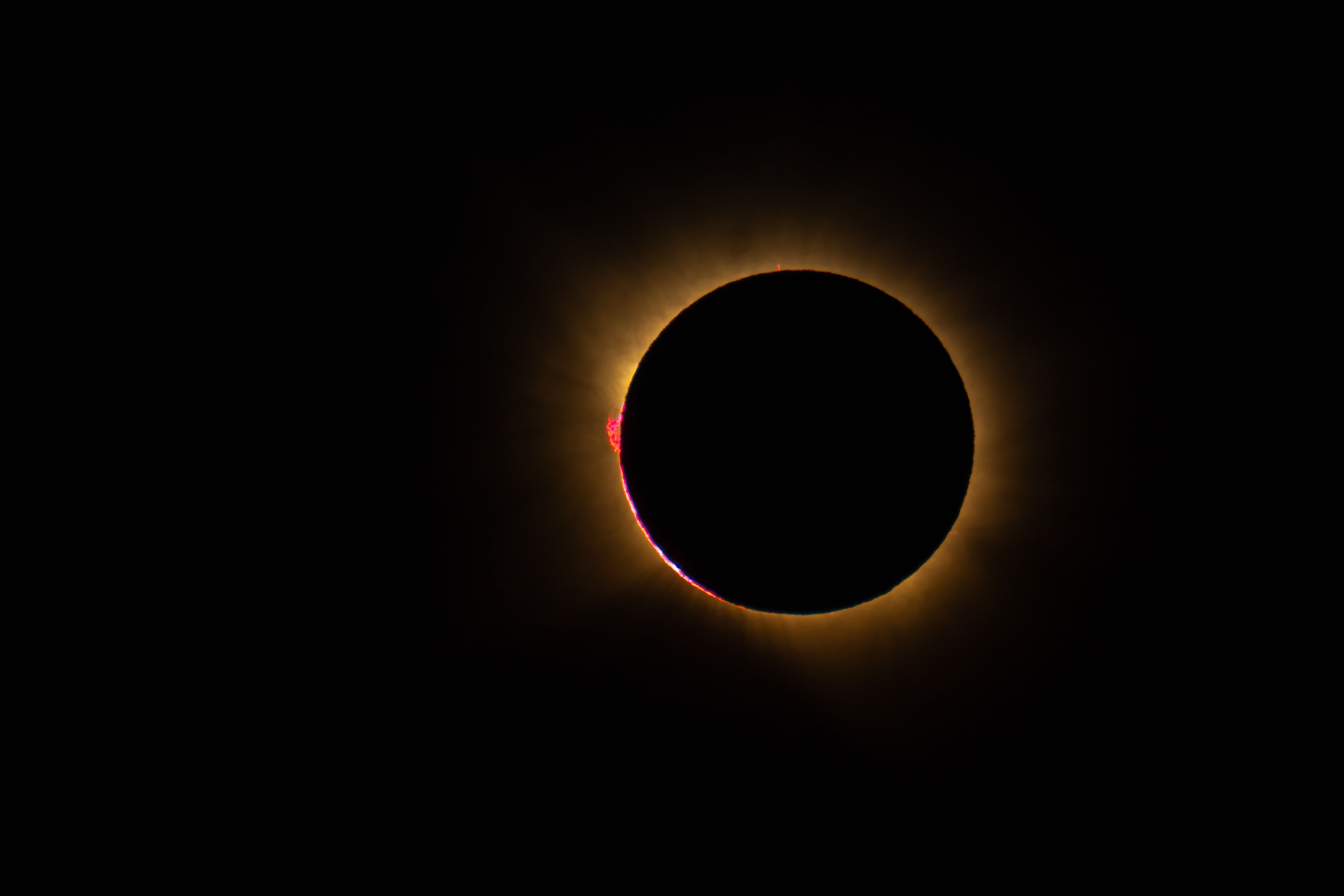 Un eclipse solar total con la corona brillante y prominencias rojas visibles en los bordes.