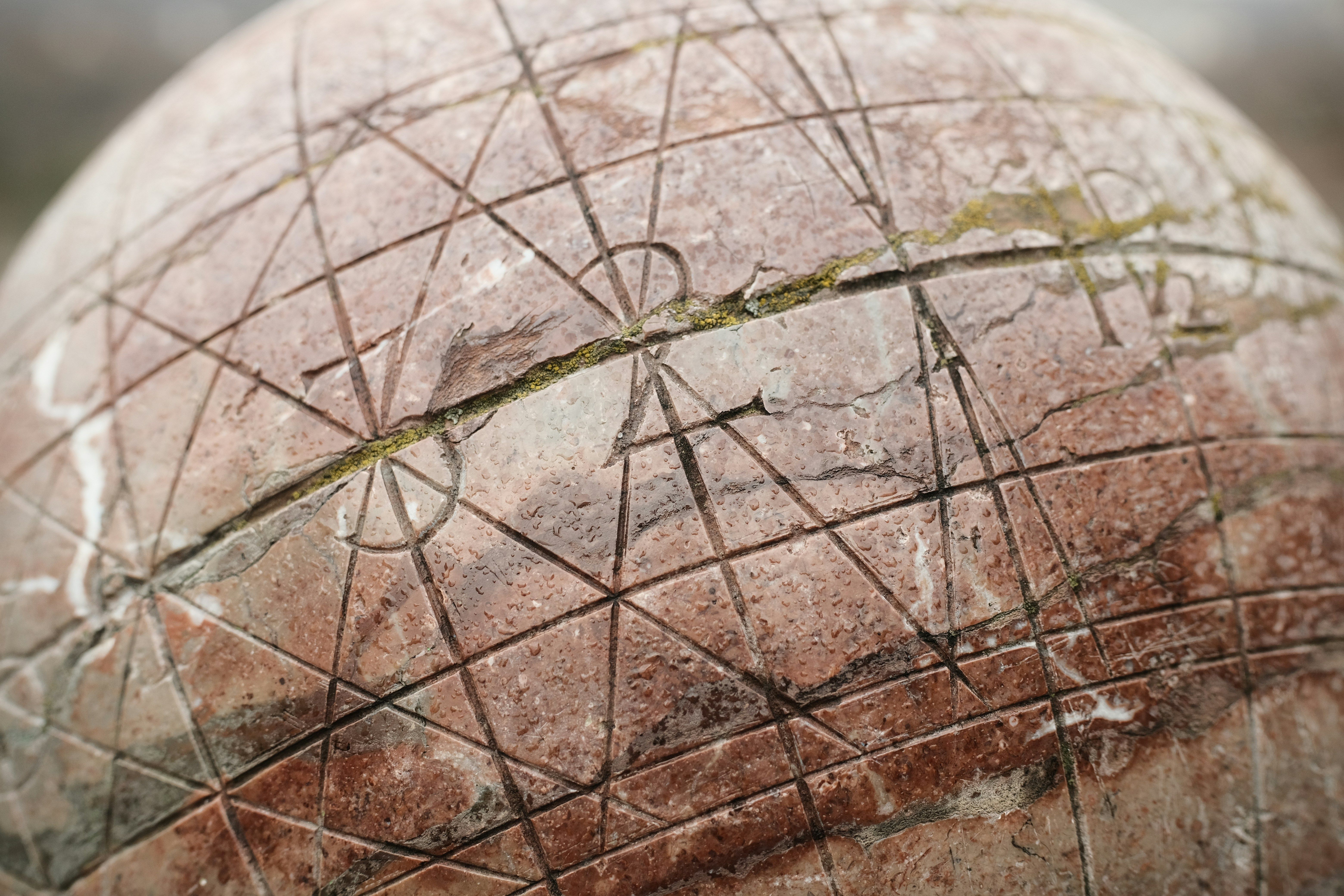 Primer plano de una esfera de piedra rojiza con grabados geométricos y una grieta central.