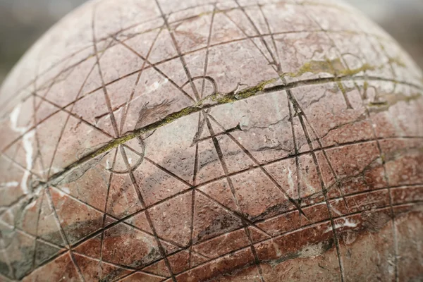 Primer plano de una esfera de piedra rojiza con grabados geométricos y una grieta central.