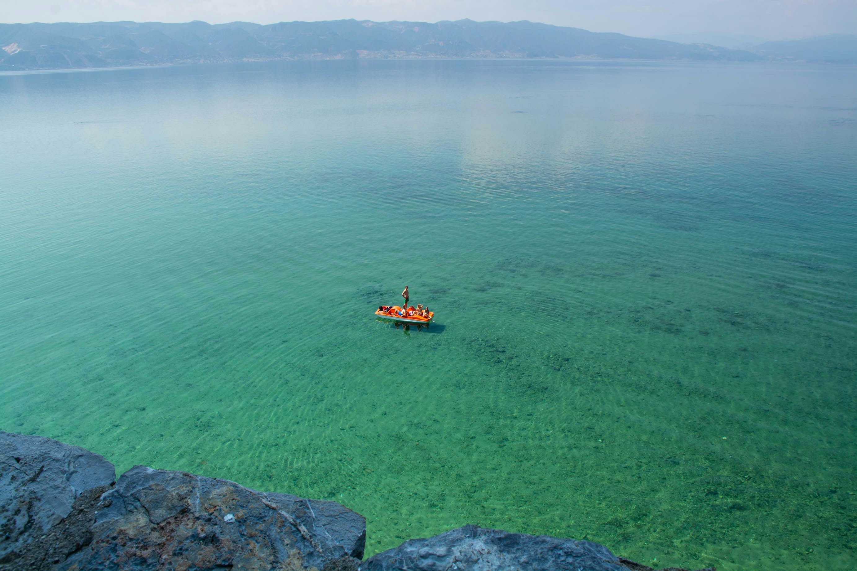 Vista aérea de un bote naranja con personas en un lago de aguas cristalinas y turquesas.