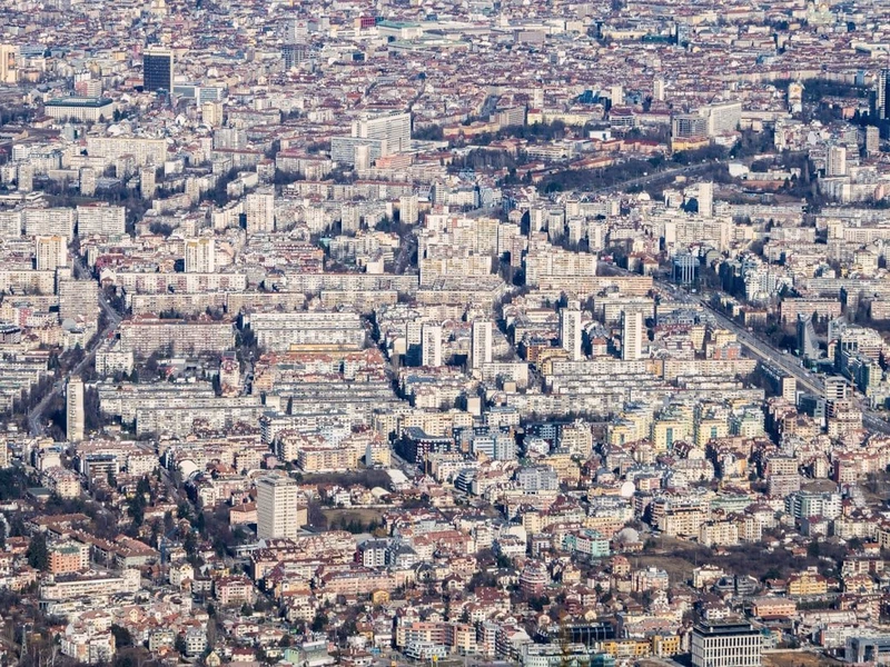 Vista aérea de Sofía con bloques de edificios grises y marrones, calles anchas y vegetación dispersa