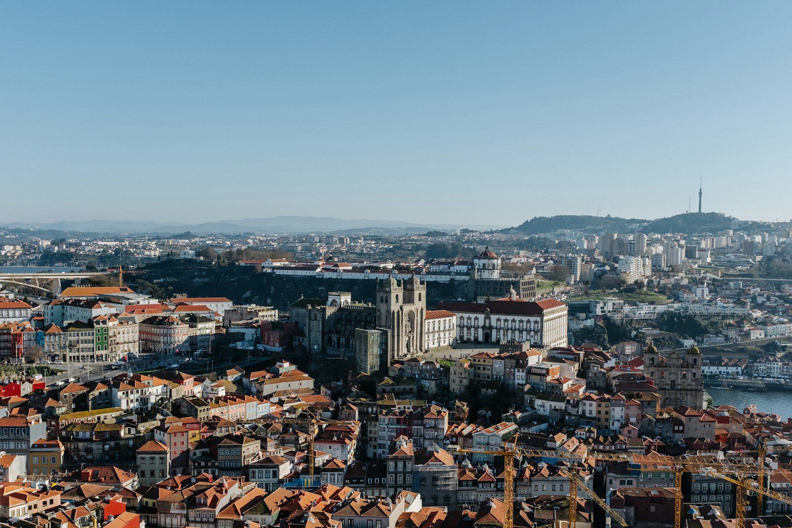 Vista panorámica de Oporto con la catedral gótica, casas de techos rojos junto al río Duero y puente icónico, bajo cielo azul claro
