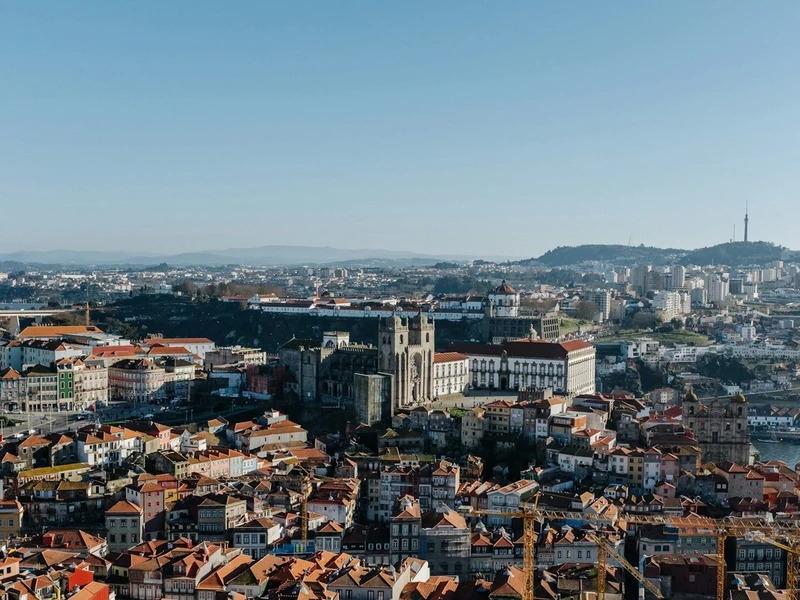 Vista panorámica de Oporto con la catedral gótica, casas de techos rojos junto al río Duero y puente icónico, bajo cielo azul claro