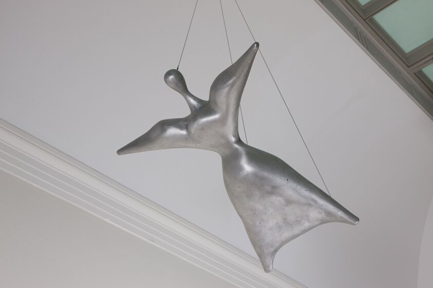 Escultura abstracta plateada colgando del techo, con formas orgánicas y líneas suaves.