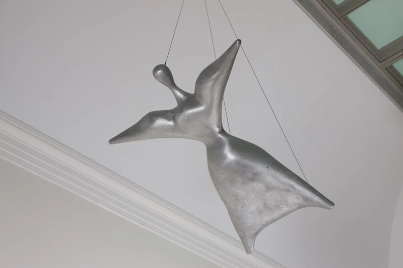 Escultura abstracta plateada colgando del techo, con formas orgánicas y líneas suaves.