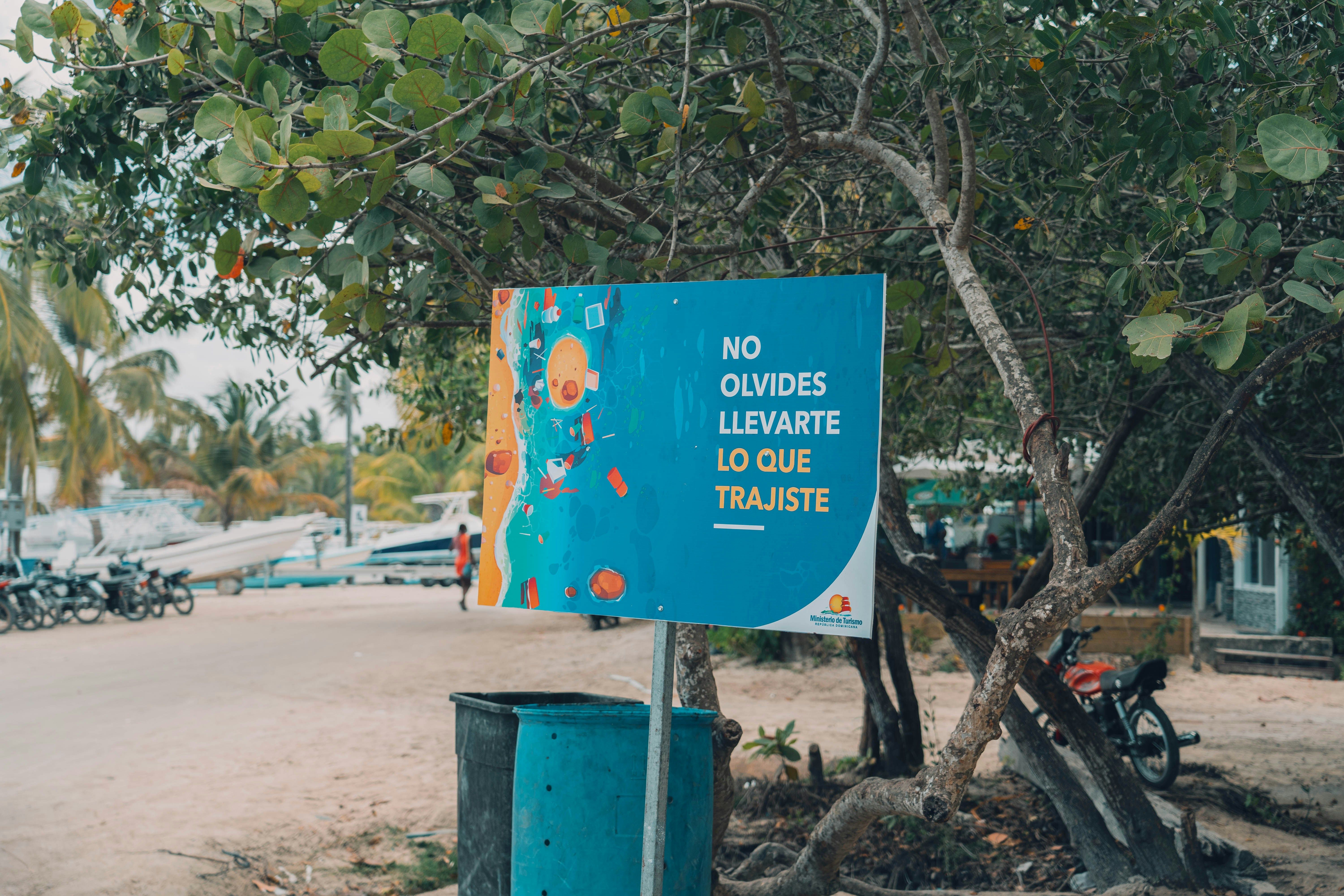 Cartel azul con mensaje "No olvides llevarte lo que trajiste" junto a un cubo de basura en una playa.