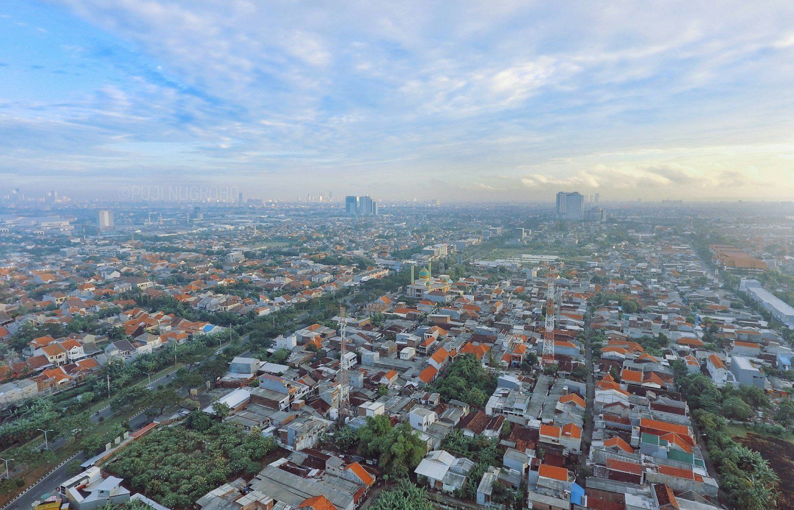Vista aérea de la ciudad de Bali con edificios de techos rojos, calles urbanas y cielo nublado al atardecer