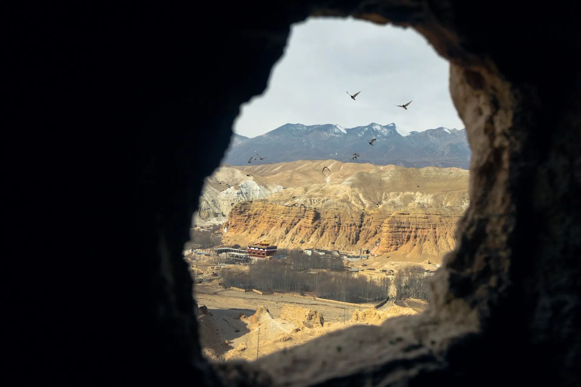 Vista de un paisaje desértico montañoso con acantilados y aves volando, enmarcada por una abertura rocosa oscura.