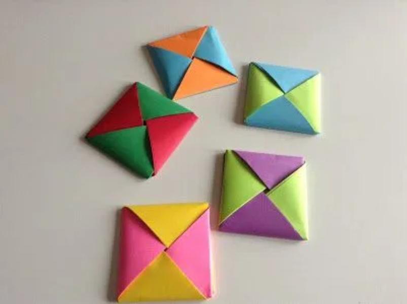 Varios ddakji de papel plegado en colores vibrantes: naranja, azul, verde, rojo, amarillo, púrpura y rosa, sobre fondo blanco