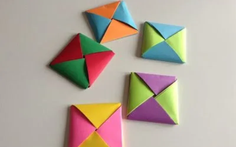 Varios ddakji de papel plegado en colores vibrantes: naranja, azul, verde, rojo, amarillo, púrpura y rosa, sobre fondo blanco