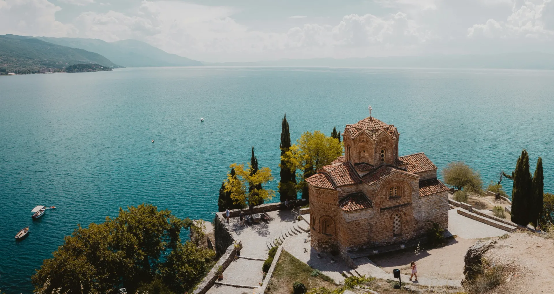 Vista aérea de una iglesia de piedra con tejado de tejas rojas junto a un gran lago azul.