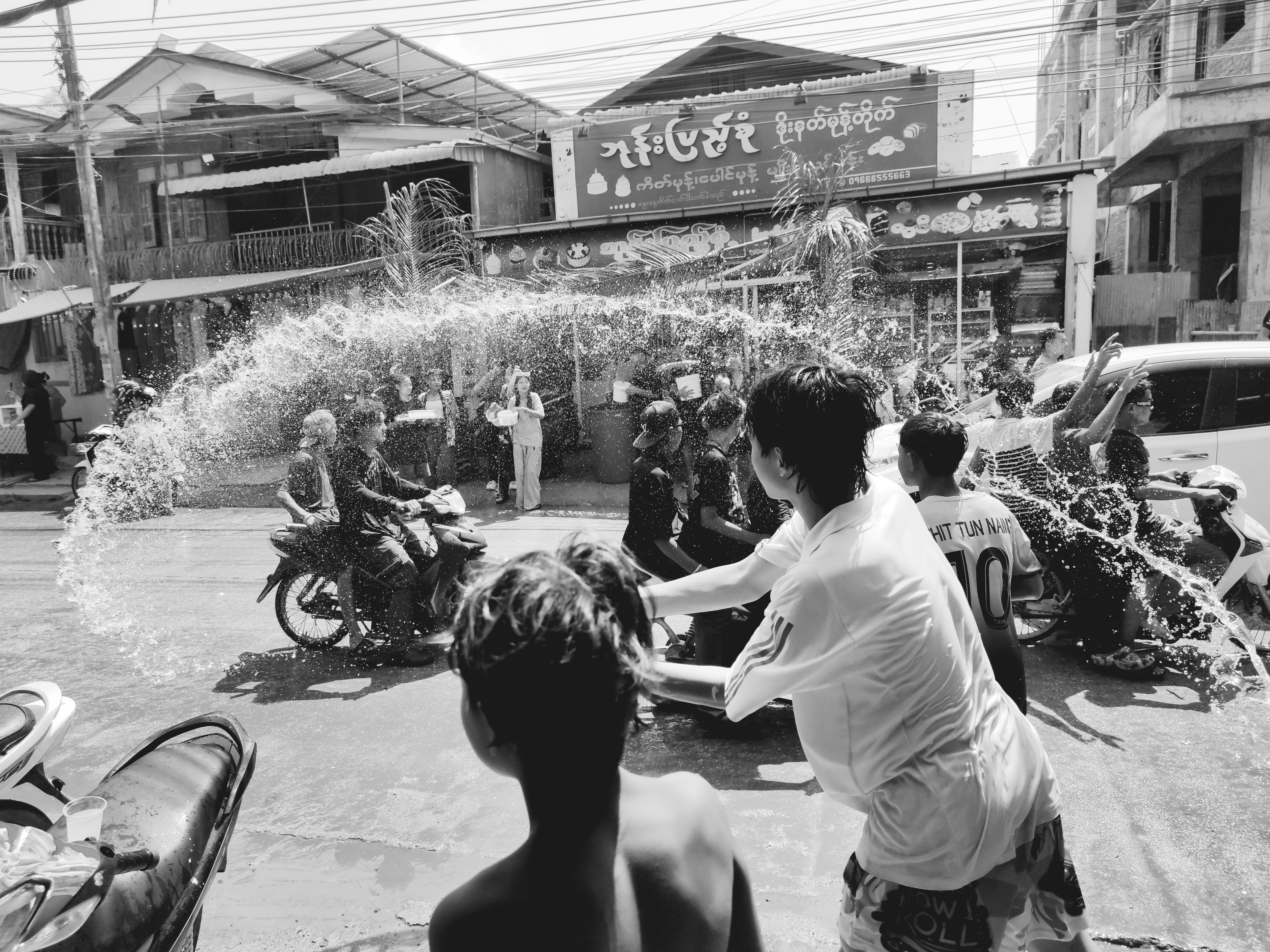 Personas lanzando agua en una calle con edificios al fondo, en blanco y negro.