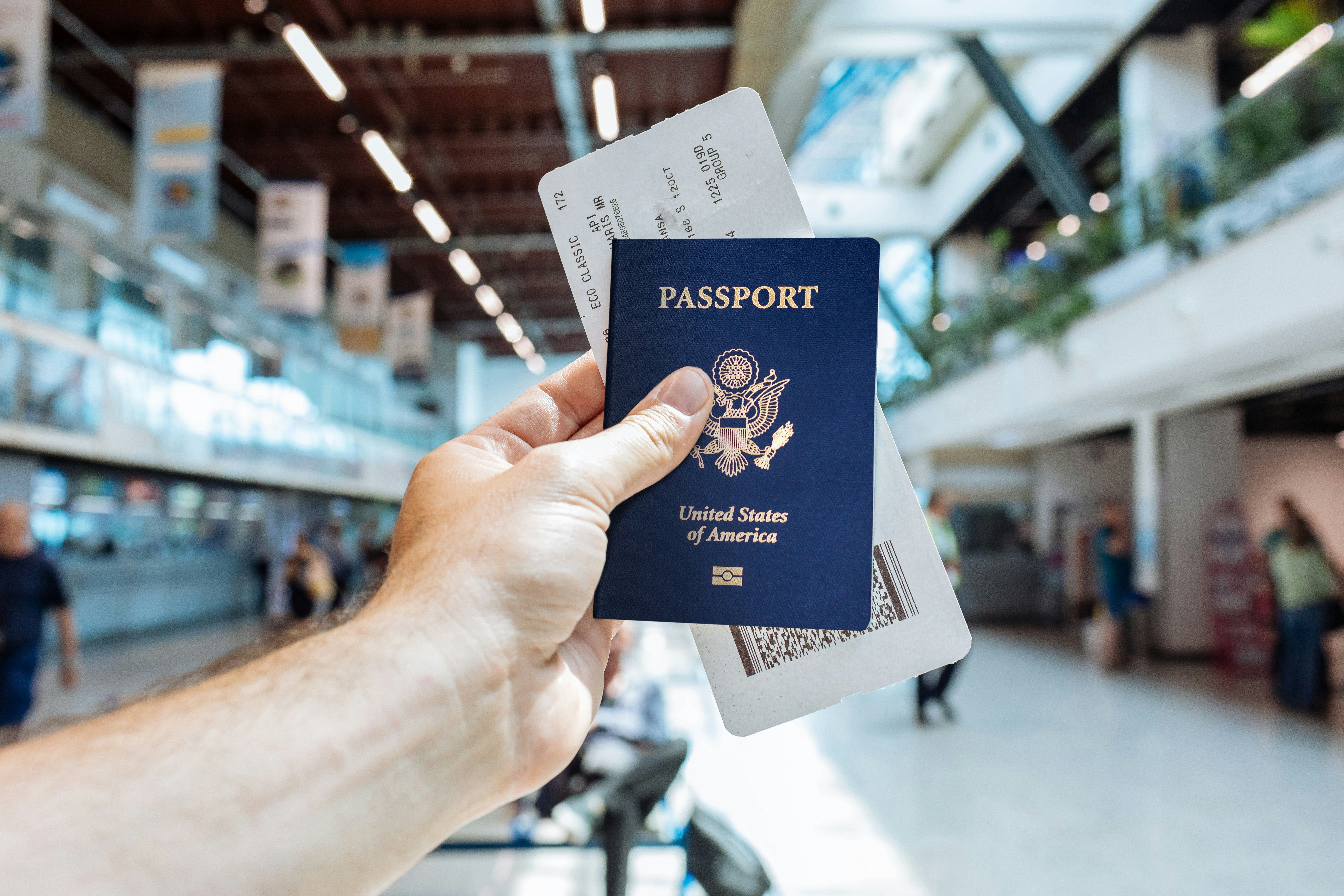 Mano sosteniendo un pasaporte de Estados Unidos y un billete de avión en un aeropuerto.