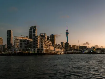 Panorama del skyline de Auckland al atardecer, con la torre Sky Tower iluminada en azul y edificios modernos junto al puerto
