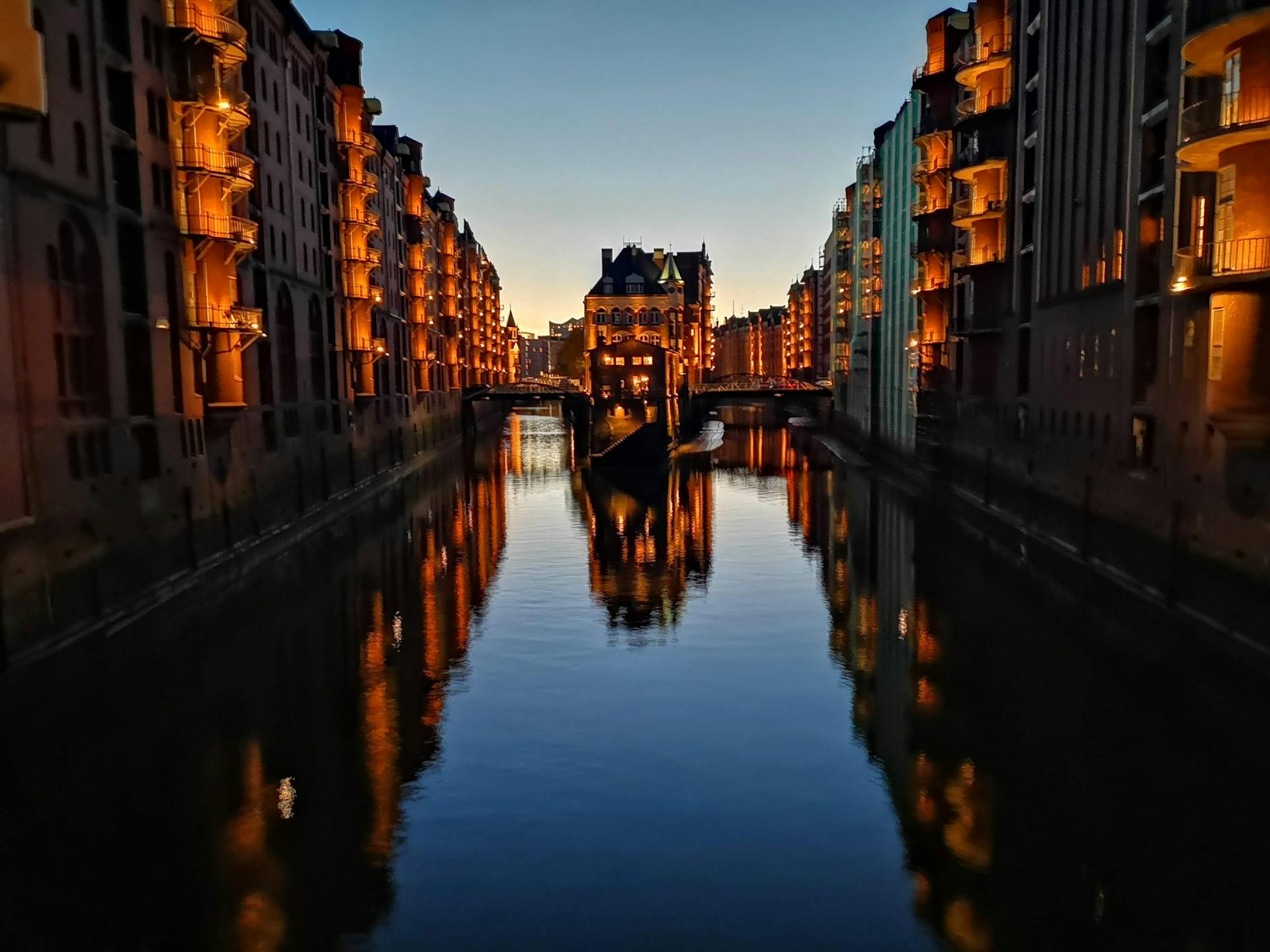 Vista del canal en Speicherstadt, Hamburgo, al atardecer, con edificios de ladrillo iluminados y reflejos en el agua