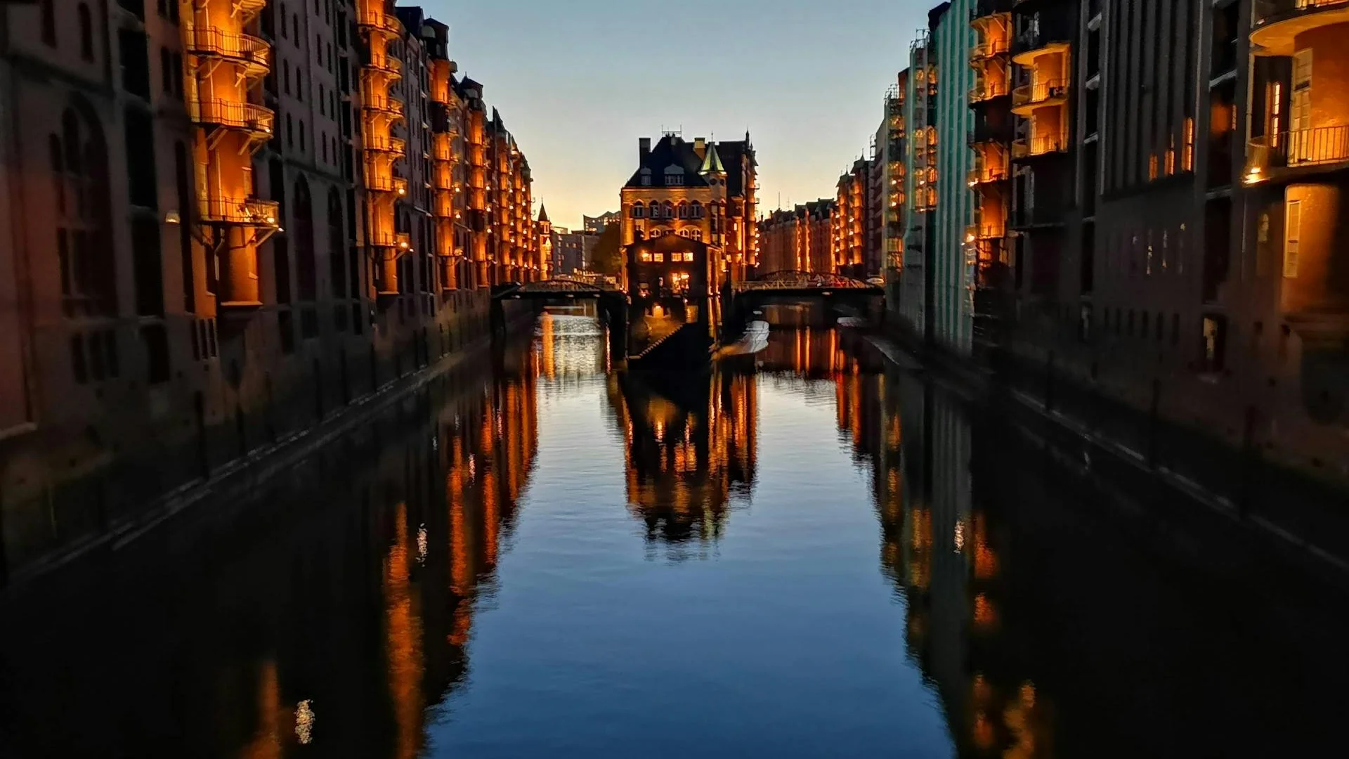 Vista del canal en Hamburgo con edificios históricos iluminados y reflejos en el agua al atardecer