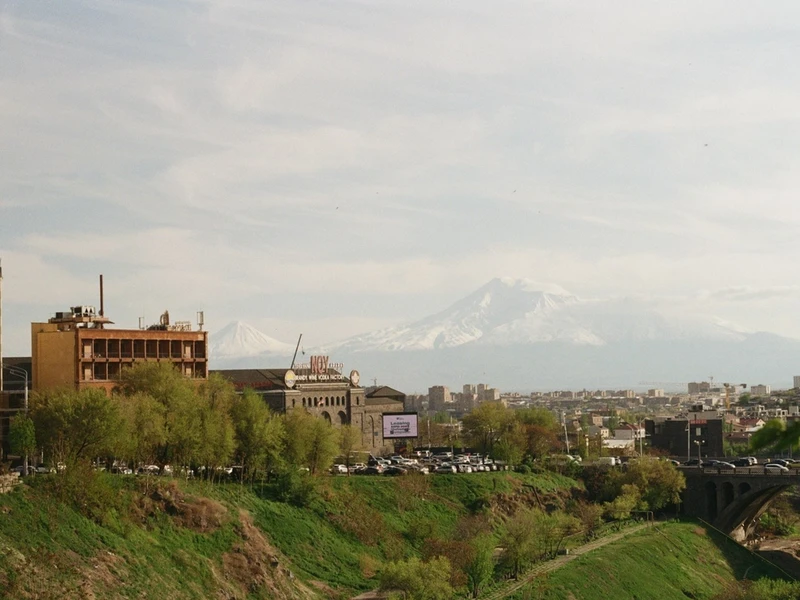 Vista panorámica de Ereván con el monte Ararat nevado al fondo, edificios antiguos junto a un río verde y puente
