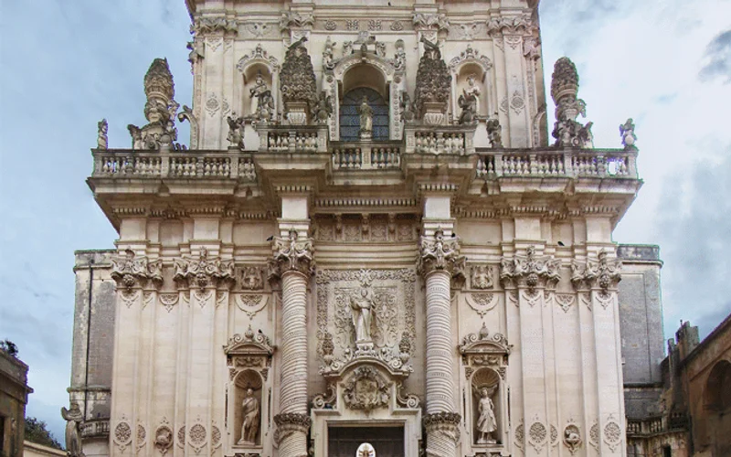 Fachada barroca de una iglesia en Lecce, con relieves escultóricos en piedra clara y cielo nublado al fondo