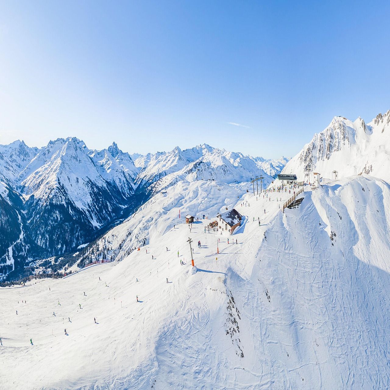 Vista aérea de una estación de esquí alpina con pistas nevadas, remontes y edificios de montaña.