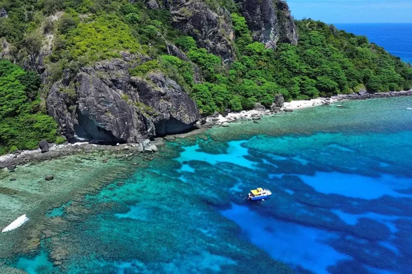 Vista aérea de acantilados verdes y playa arenosa en Denarau, Fiji, con aguas turquesas claras y un bote amarillo en el mar