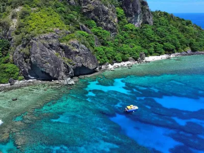 Vista aérea de acantilados verdes cubiertos de vegetación junto a una playa blanca y aguas turquesas con arrecifes y un bote amarillo en Denarau