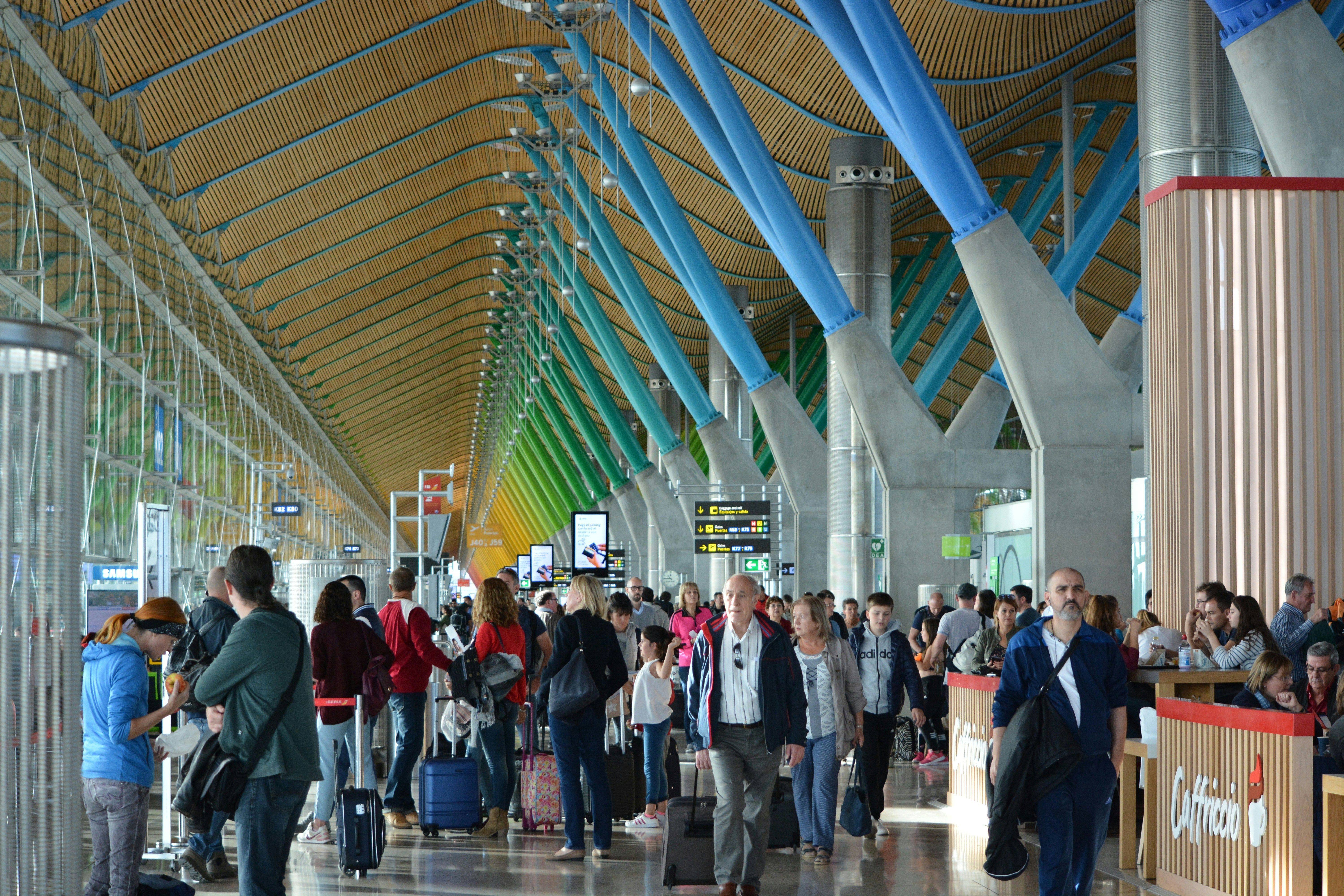 Pasajeros con equipaje de mano caminando por una terminal de aeropuerto moderna y colorida.