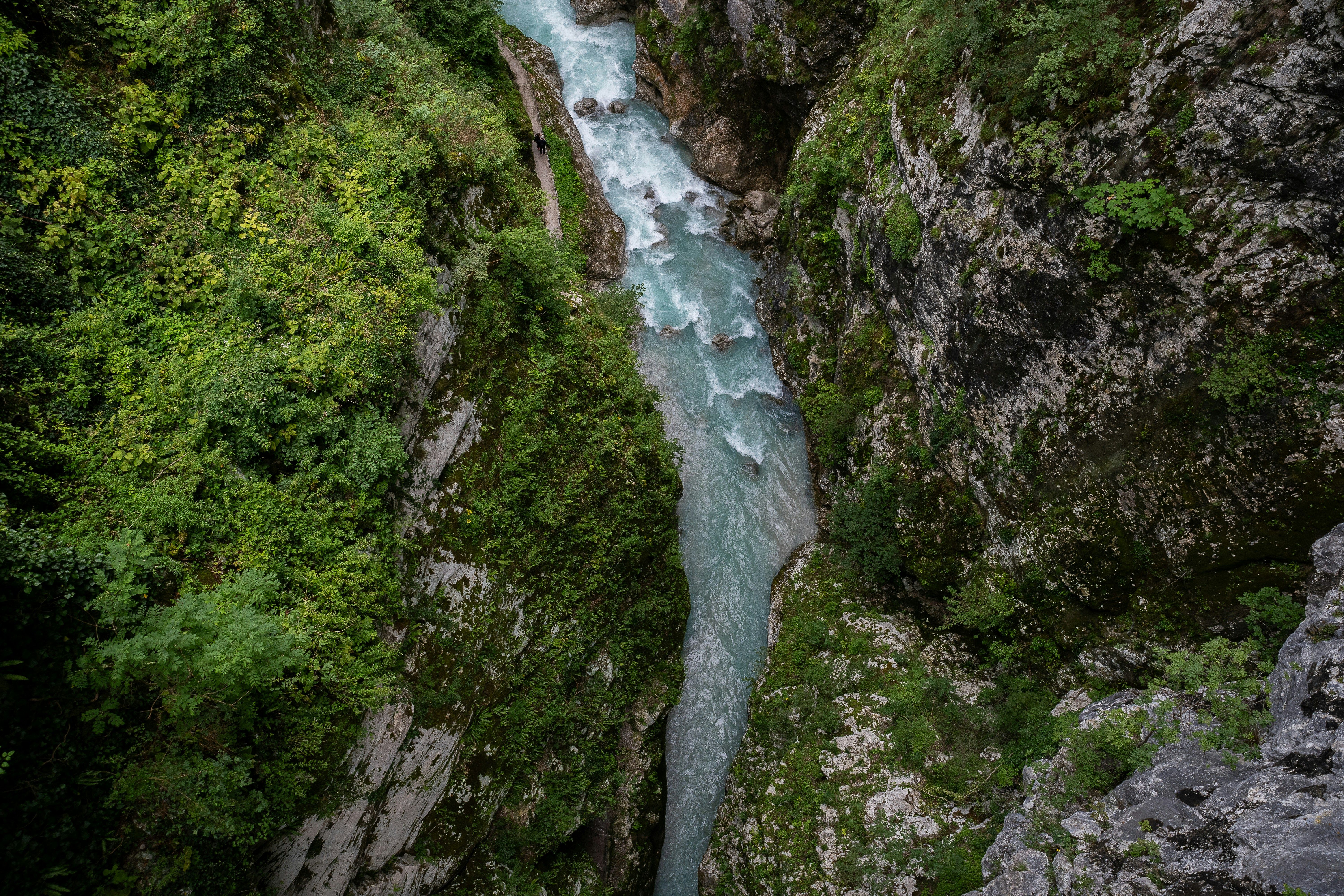 Vista aérea de un río azul turquesa serpenteando entre paredes rocosas cubiertas de vegetación verde.