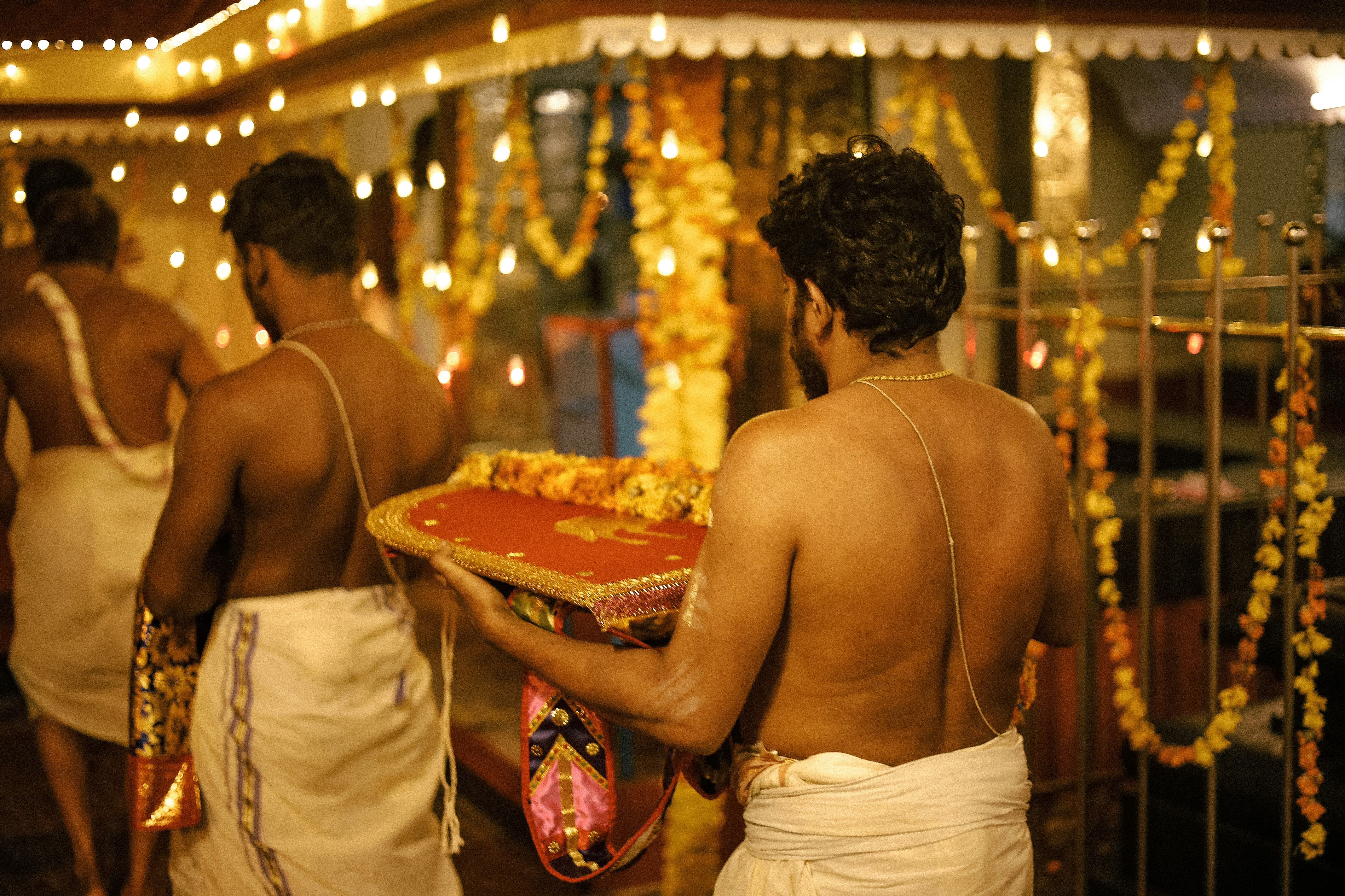 Hombres con túnicas blancas llevan ofrendas en un ritual iluminado con guirnaldas de luces.