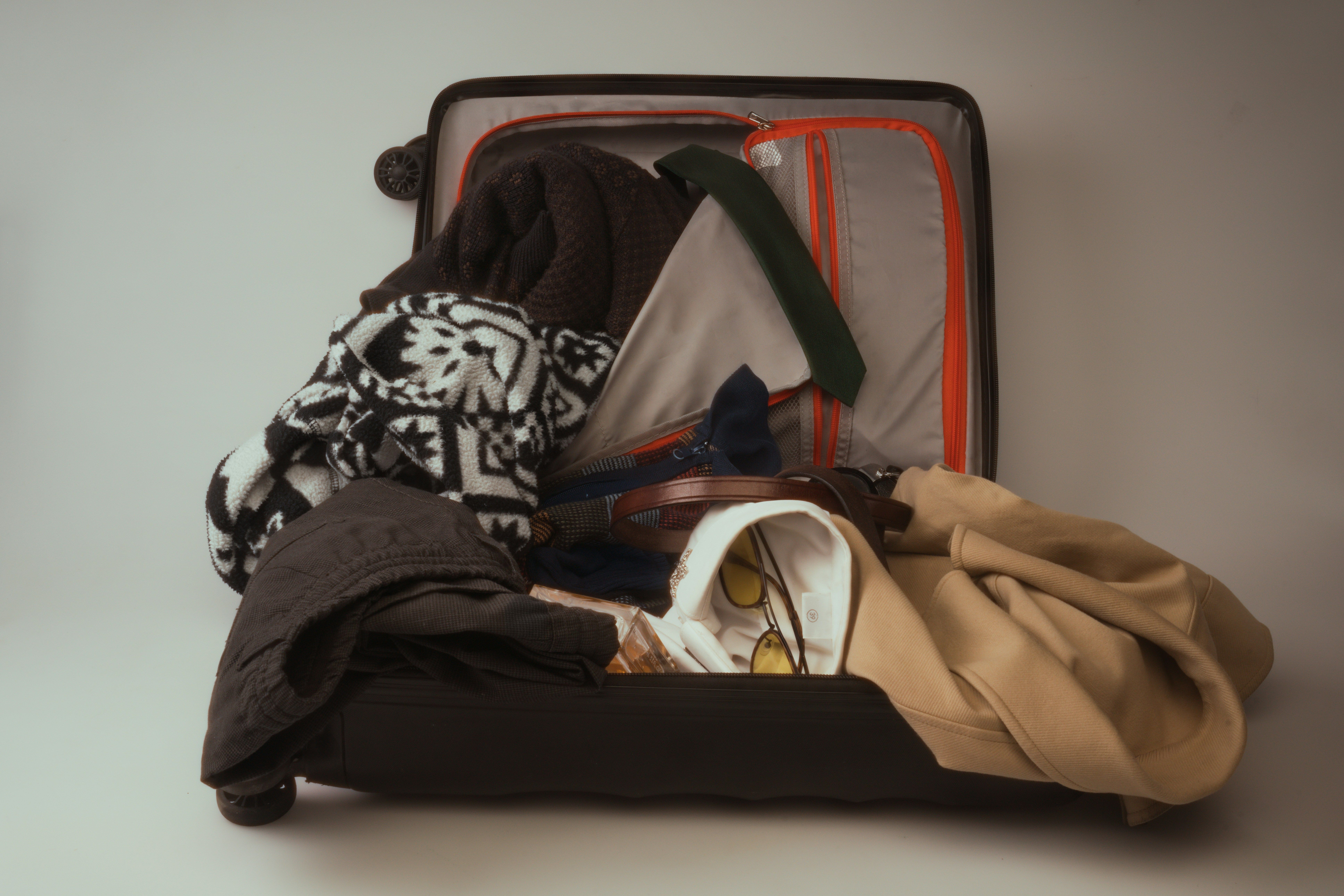 Una maleta de cabina abierta y desordenada, llena de ropa y accesorios diversos.