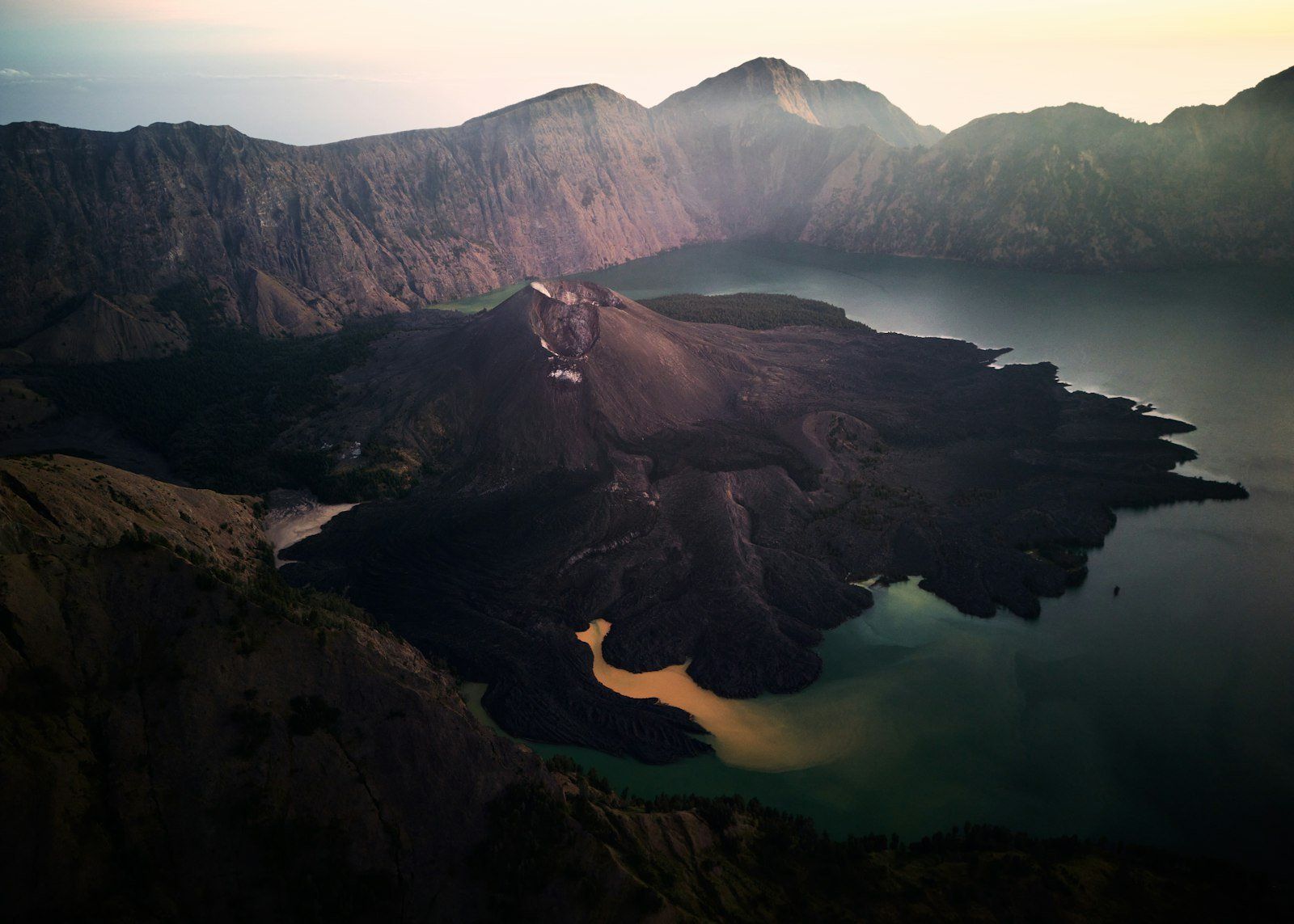 Vista aérea del volcán Rinjani en Lombok, con lago cráter de aguas turquesas y amarillas, rodeado de montañas oscuras al atardecer