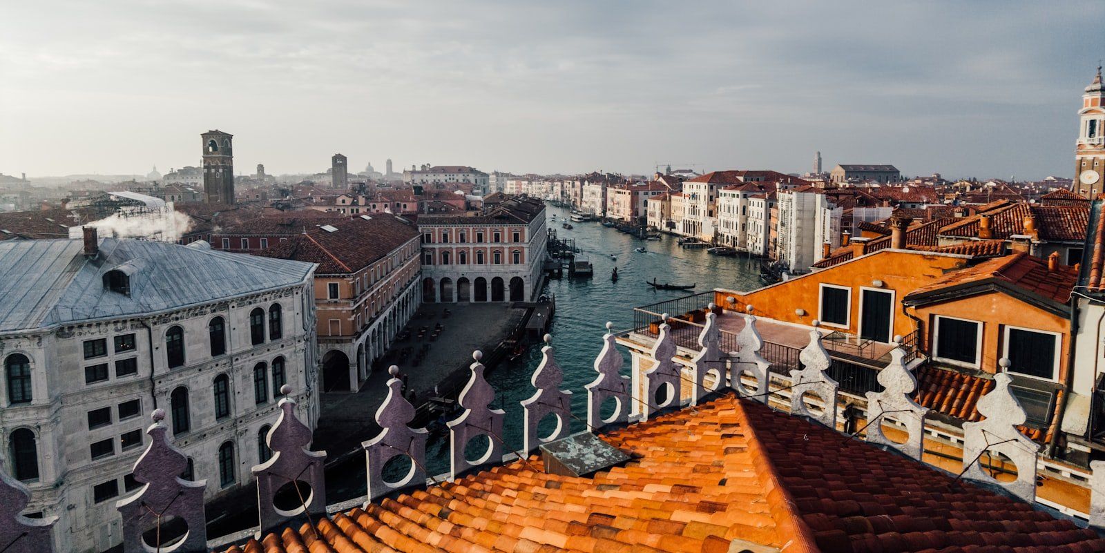 Vista panorámica de Venecia con edificios históricos de fachadas blancas y rojas junto a un canal, techos de tejas y campanarios lejanos bajo un