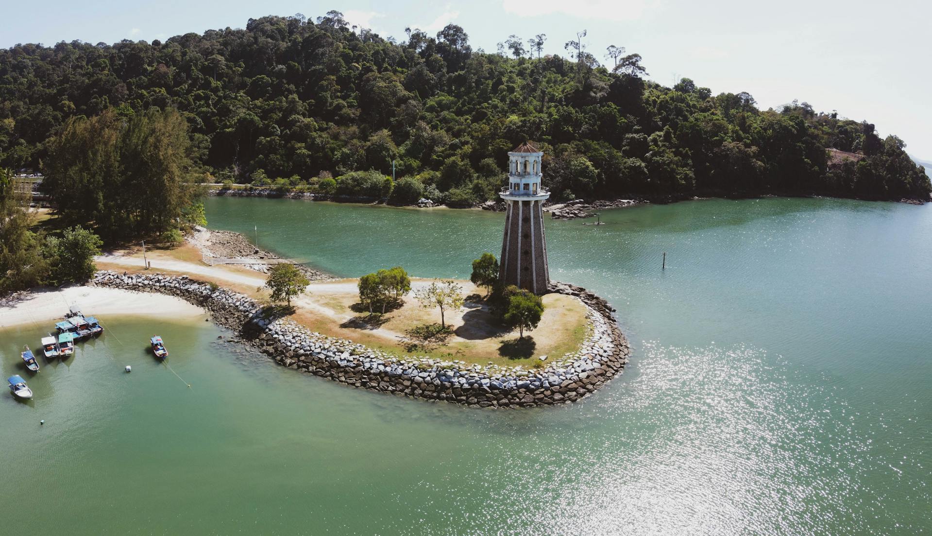 Vista aérea de un faro en una isla rocosa con vegetación tropical, playas arenosas y aguas turquesas en Langkawi