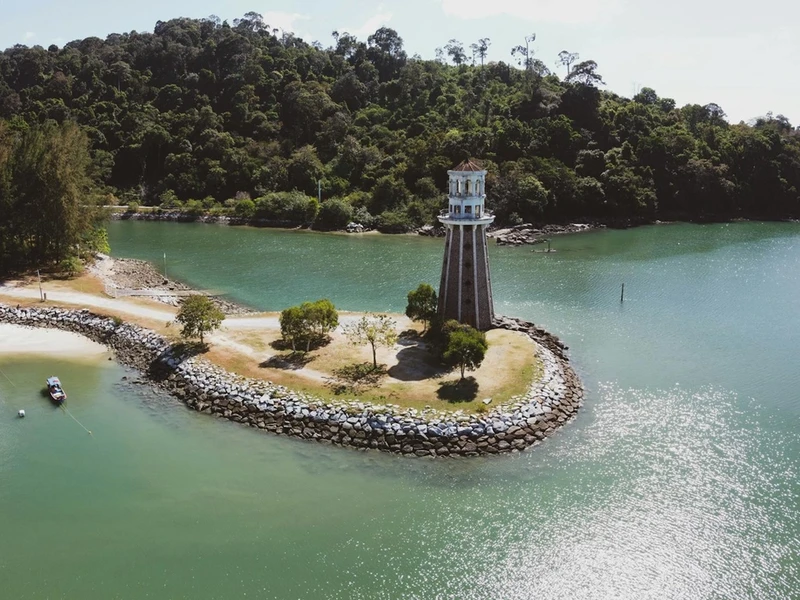 Vista aérea de un faro en una isla rocosa con vegetación tropical, playas arenosas y aguas turquesas en Langkawi