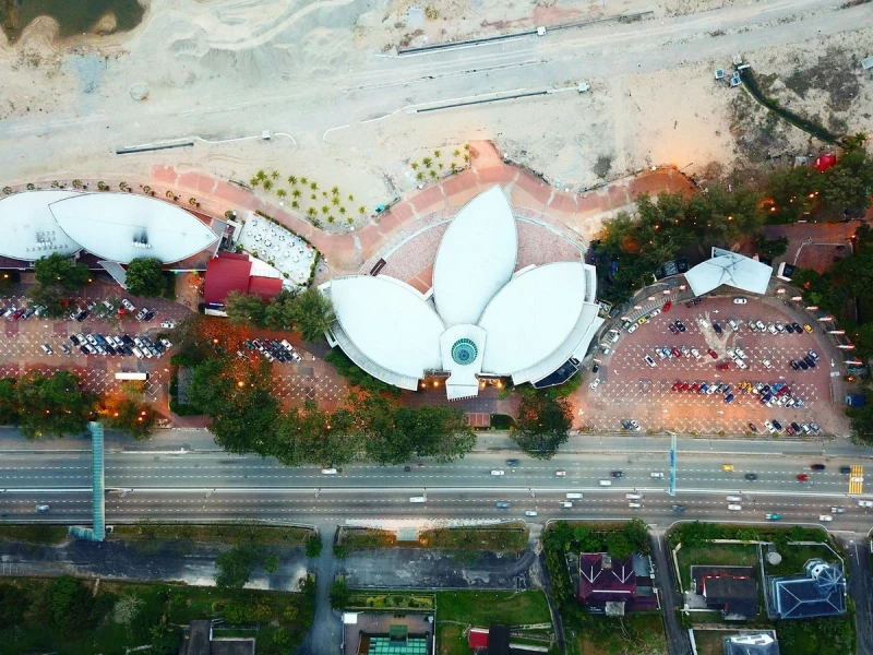 Vista aérea de un edificio blanco con forma de flor en Johor Bahru, rodeado de carreteras, vegetación y plazas pavimentadas