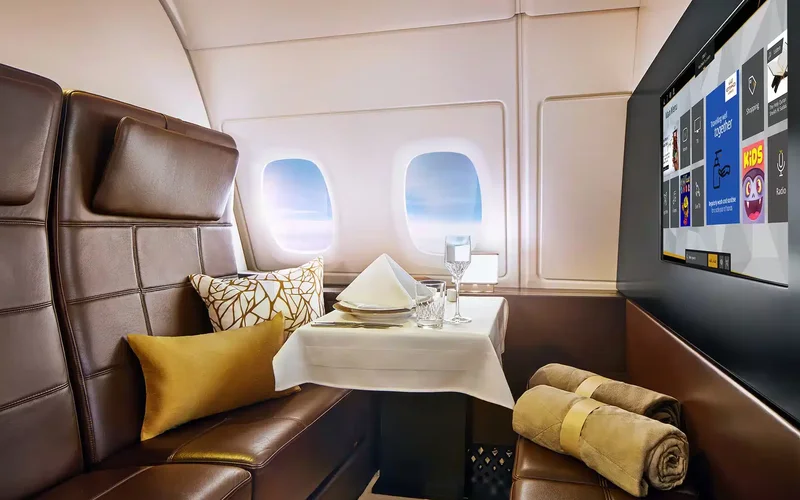 Interior lujoso de la suite The Residence en Etihad Airways, con asientos de cuero marrón, mesa con servicio de té, mantas y vistas al cielo azul
