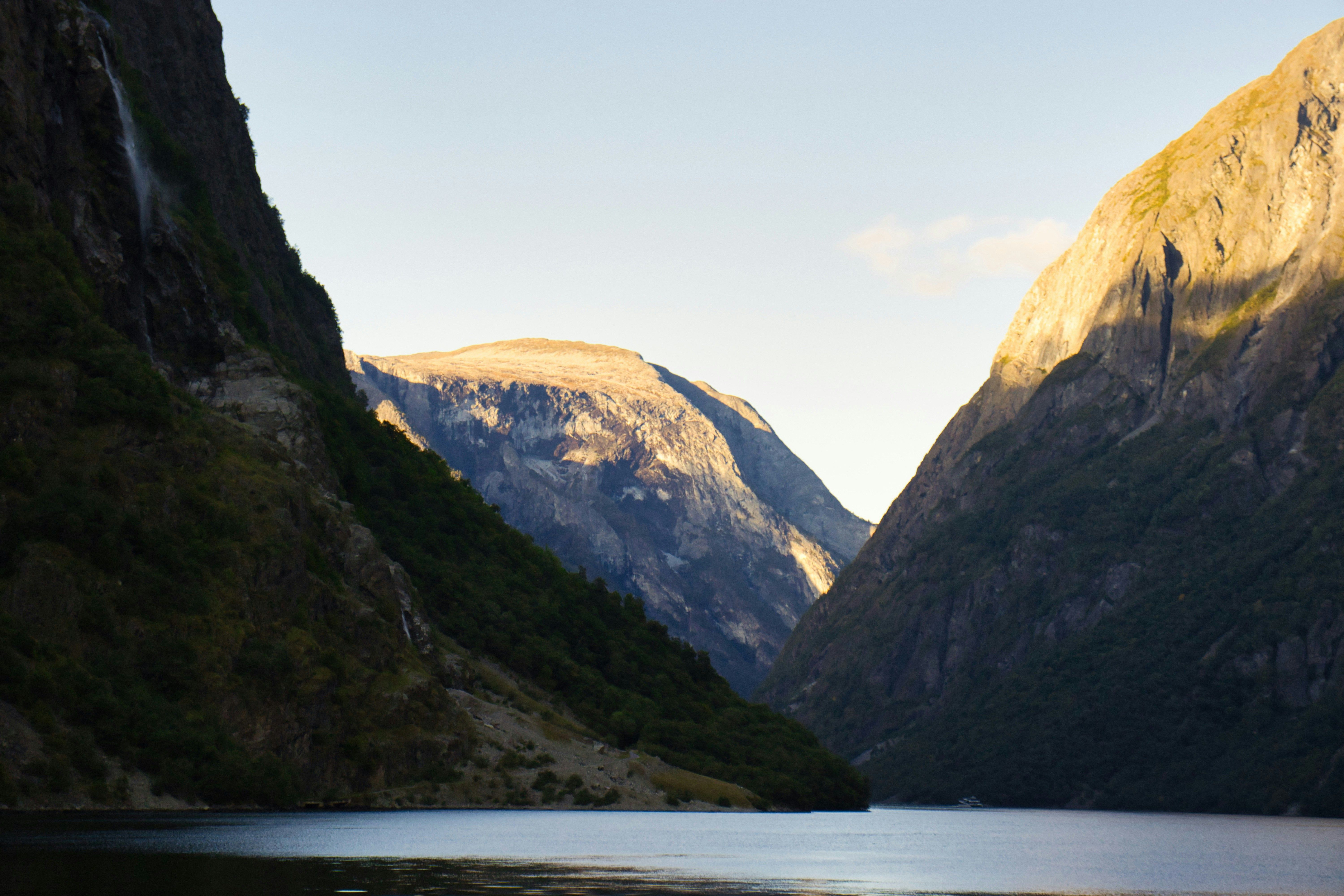 Fiordo noruego con montañas escarpadas y un cielo claro, reflejándose en el agua.