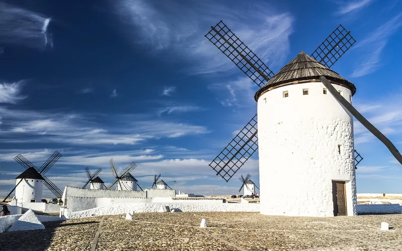 Molinos de viento blancos con aspas oscuras bajo un cielo azul con nubes dispersas.