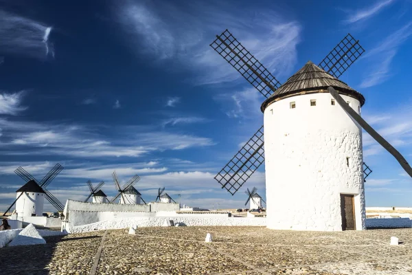 Molinos de viento blancos con aspas oscuras bajo un cielo azul con nubes dispersas.