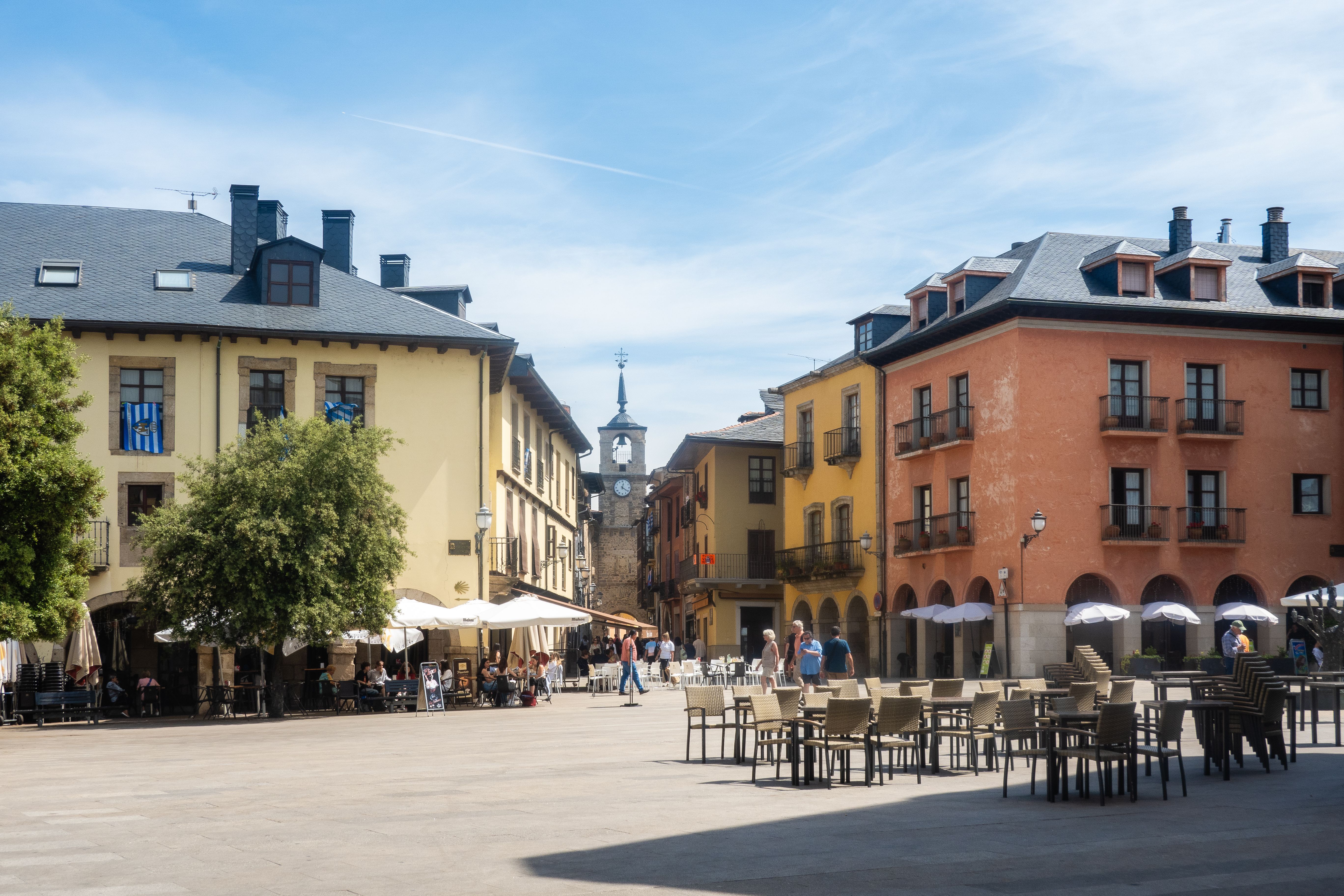 Plaza de ciudad con edificios de colores, terrazas de restaurantes y un campanario al fondo.