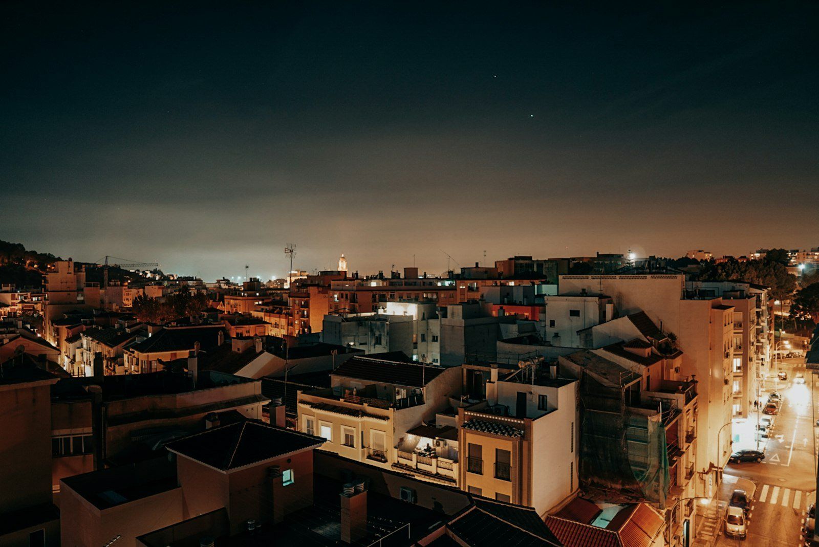 Vista nocturna de los edificios iluminados de Málaga, con calles transitadas y cielo estrellado sobre colinas