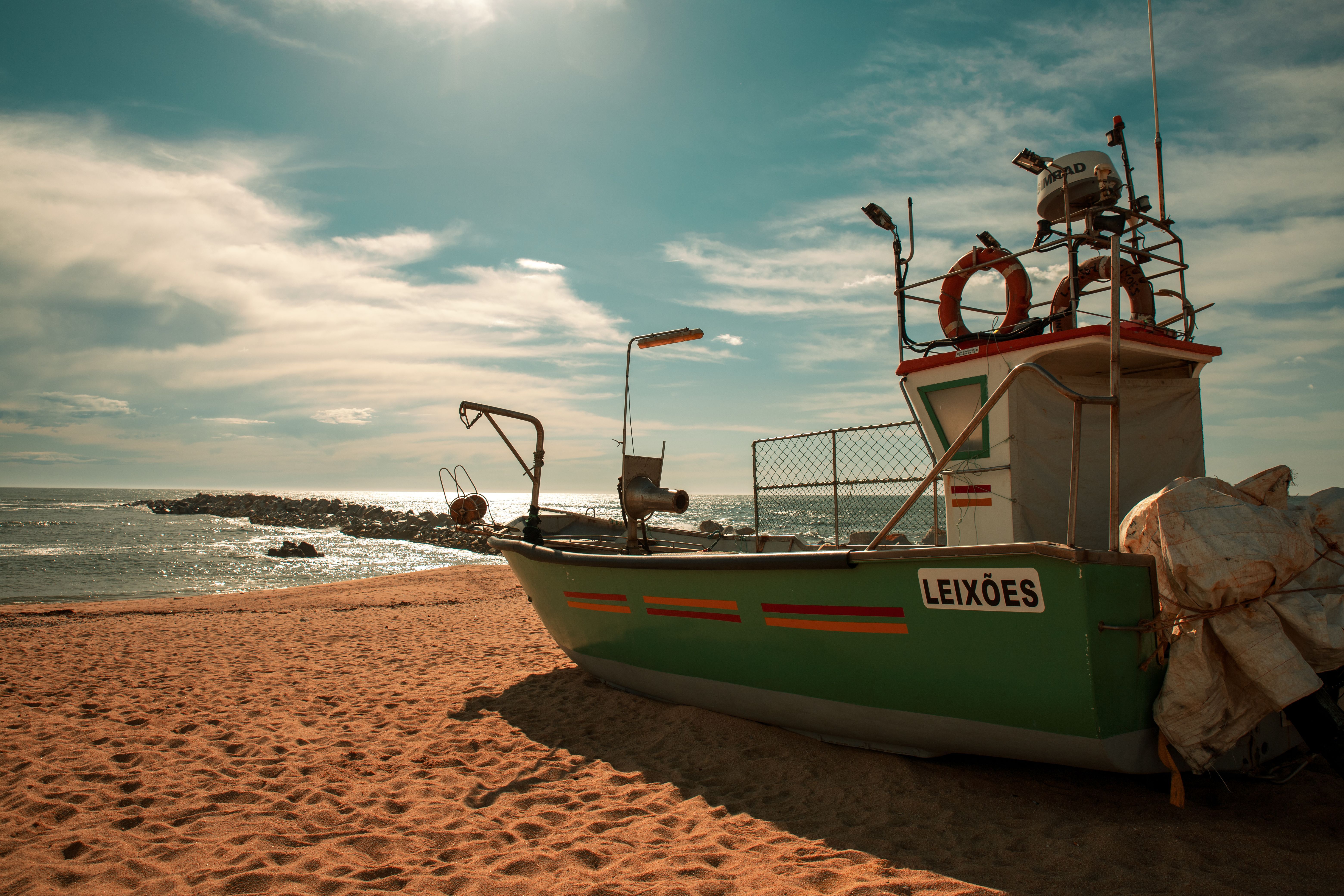 Un barco de pesca verde y blanco varado en una playa de arena bajo un cielo azul con nubes.