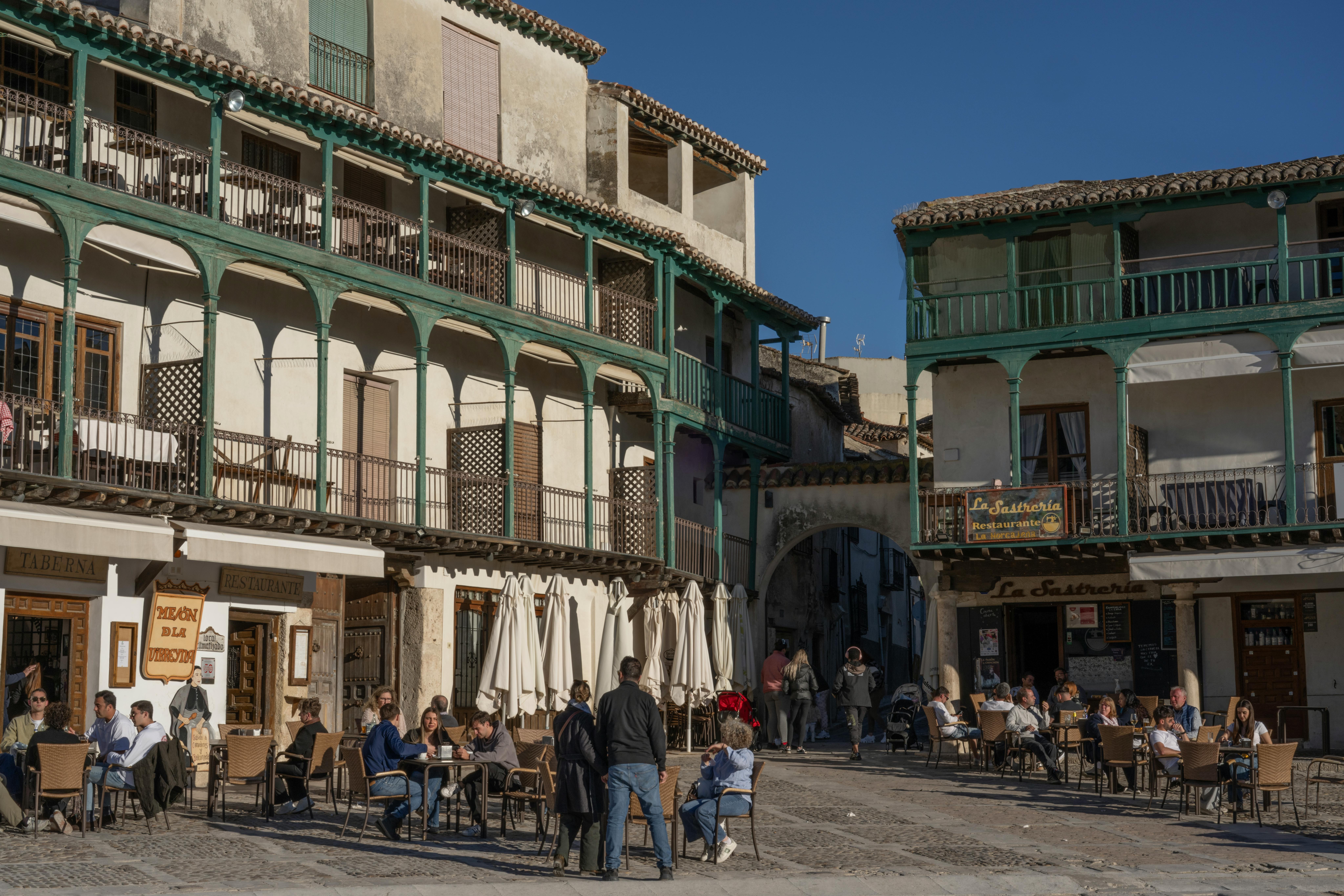 Plaza de pueblo con edificios de balcones de madera y gente sentada en terrazas de bares.