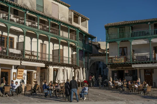 Plaza de pueblo con edificios de balcones de madera y gente sentada en terrazas de bares.