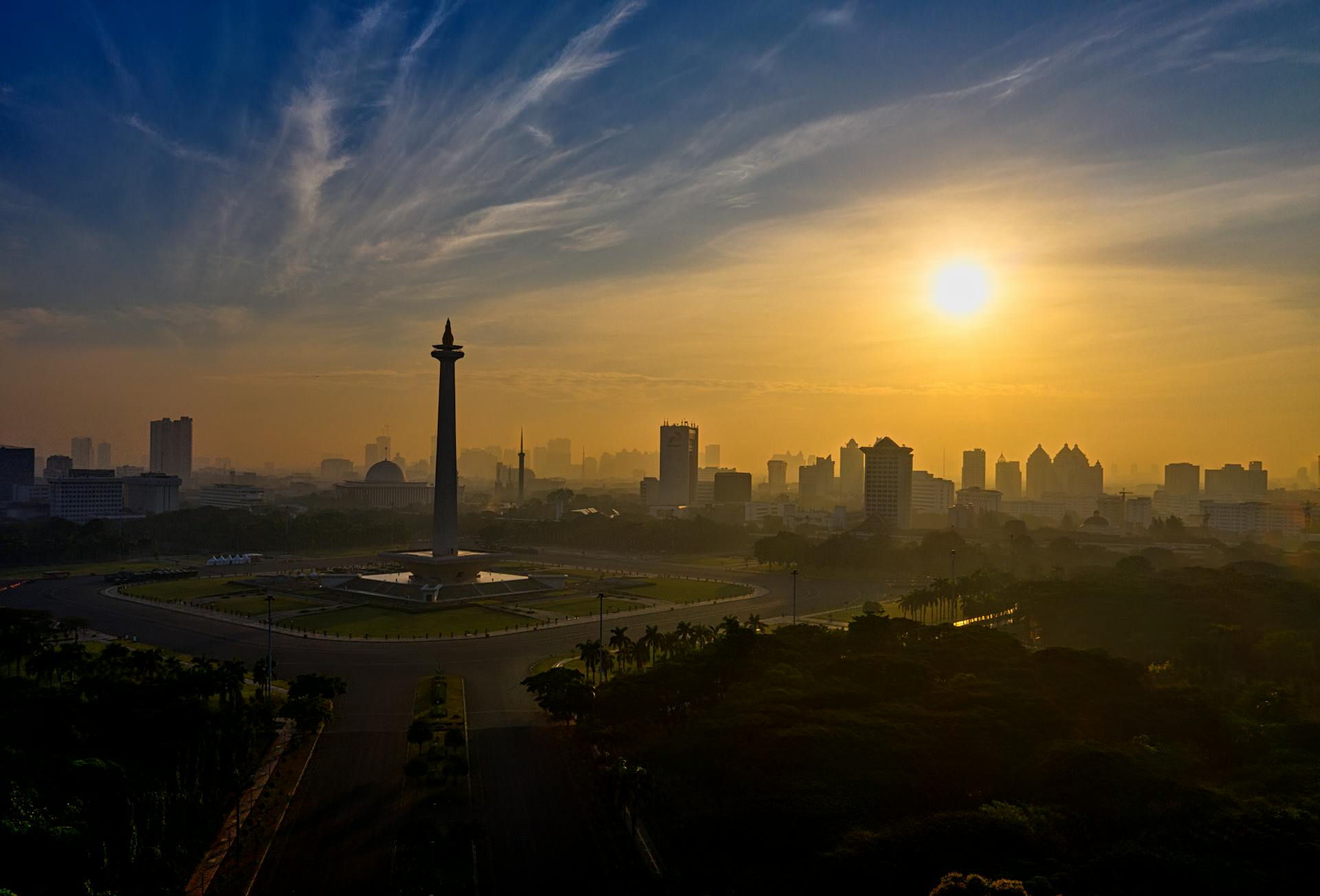 Vista panorámica de Yakarta al atardecer con el obelisco del monumento nacional en el centro, rascacielos modernos y vegetación alrededor