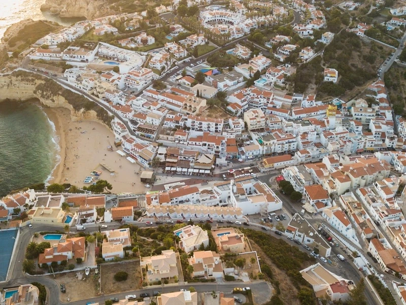 Vista aérea de Faro al atardecer, con edificios blancos de techos rojos en acantilados, playa dorada y mar azul