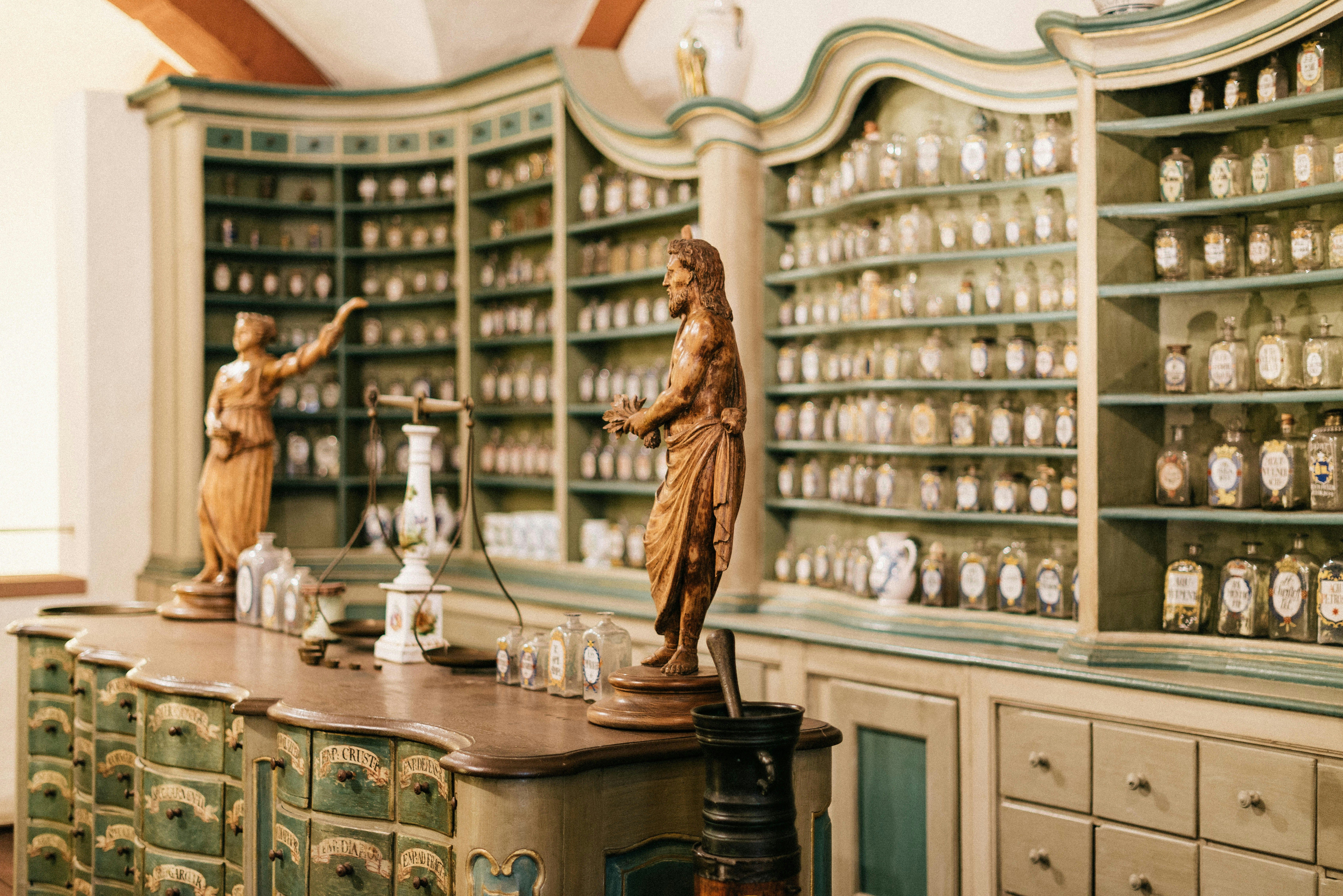 Interior de una antigua farmacia con estanterías llenas de frascos de vidrio y figuras de madera.
