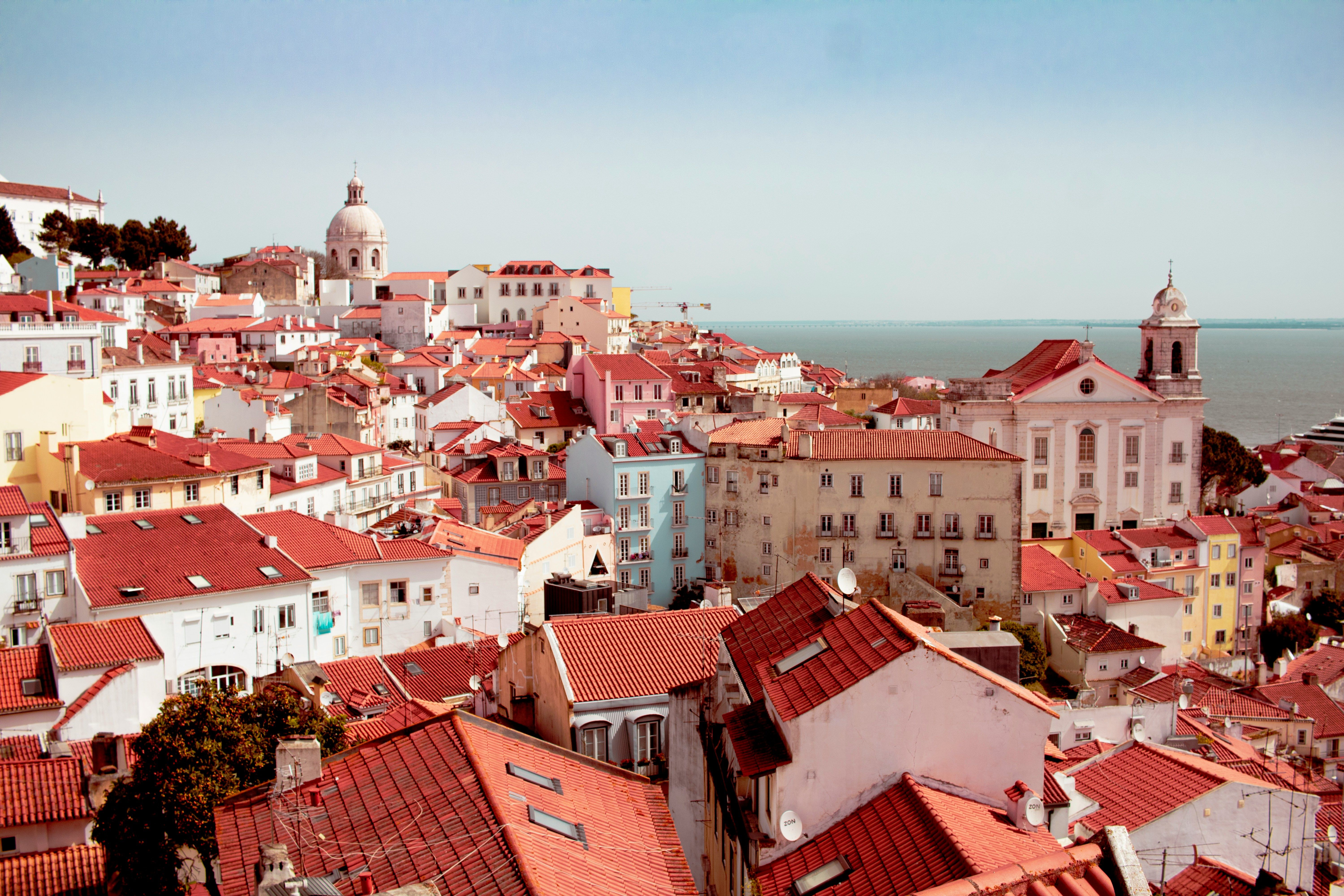 Vista aérea de tejados rojos y edificios coloridos en una ciudad costera con cúpulas y el mar al fondo.